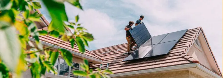 two men installing solar panels on the roof of a home