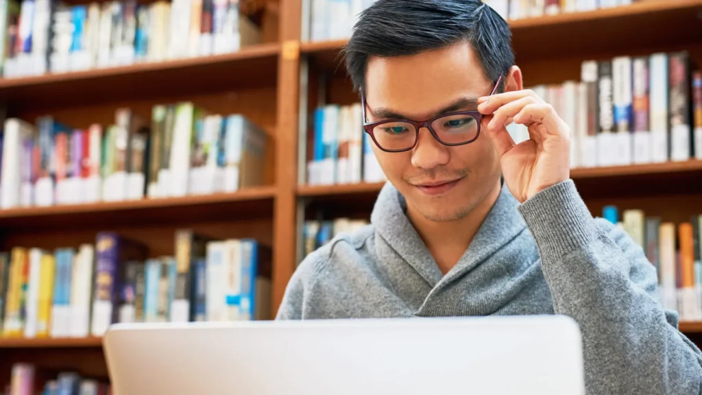 young man looking at laptop in library